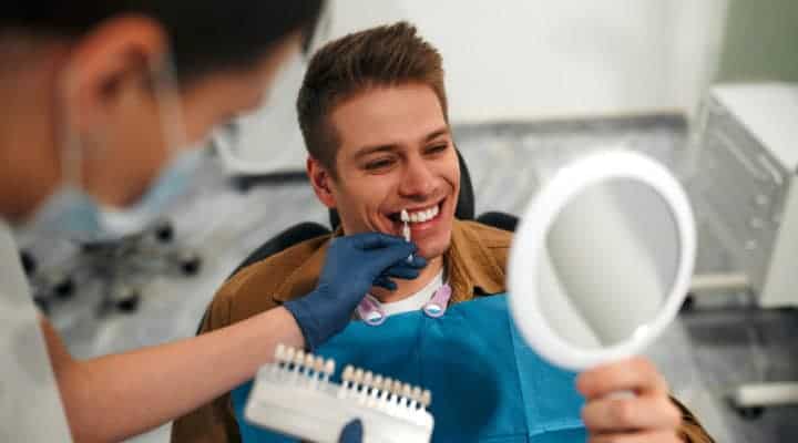 Dental hygienist matching veneers to colour of man's natural teeth