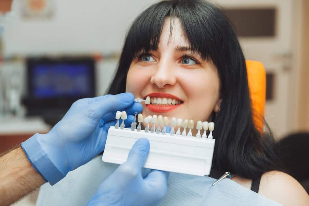 Dentist matching colour of porcelain veneers to woman's natural teeth