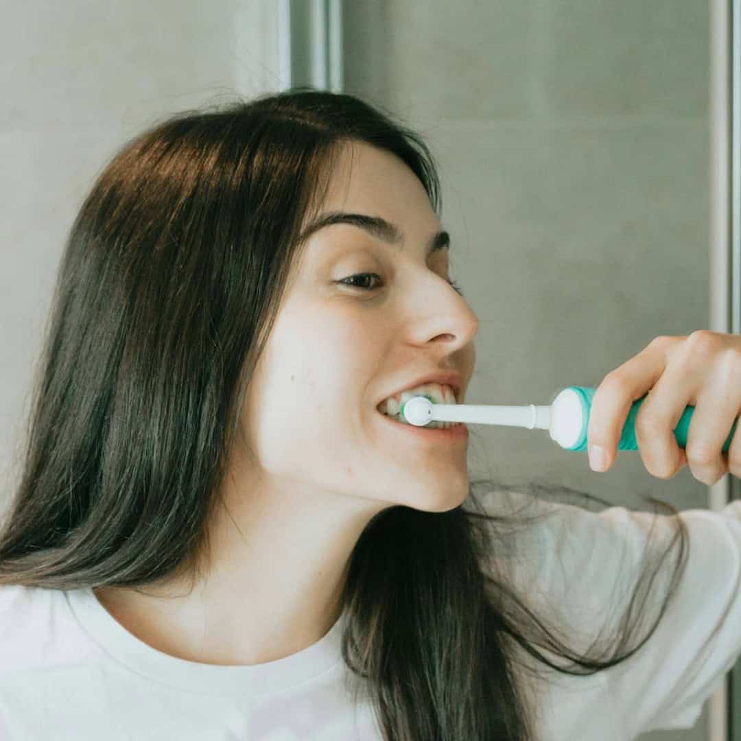 woman brushing teeth in front of mirror with electric toothbrush